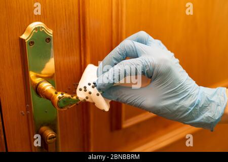 Donna che pulisce la manopola della porta della casa e usa un panno disinfettante Foto Stock