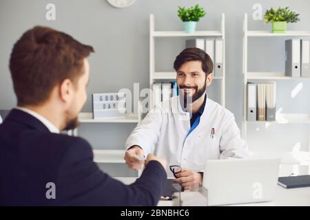 Un medico sicuro dà al paziente una prescrizione mentre si siede a un tavolo in un ufficio di clinica. Medico consultazione prescrizione diagnosi incontro con Foto Stock