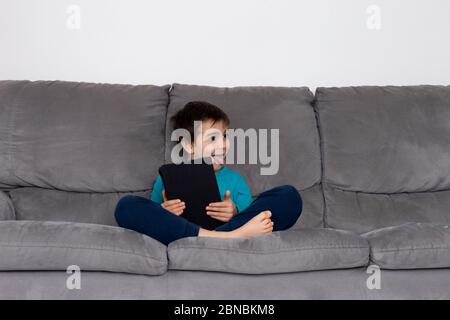 Ragazzo con tablet PC seduto sul divano, bambini che utilizzano la tecnologia, istruzione a casa, bambino che studia da casa. Ragazzo felice di stare a casa. Formazione online a distanza. Fare i compiti a scuola Foto Stock