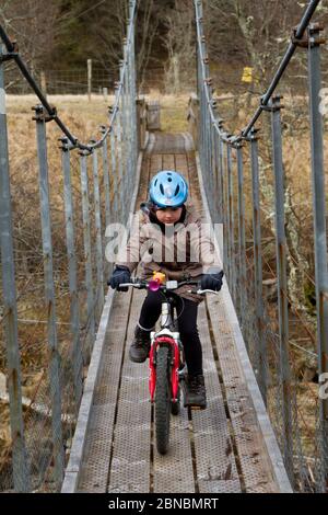 Giovane ragazza in bicicletta attraverso un ponte pedonale, Highland Scotland Foto Stock