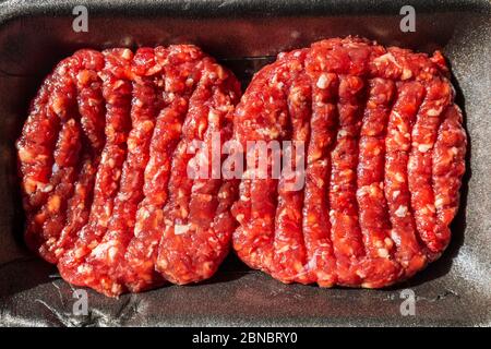 Hamburger di manzo crudo in un vassoio di confezionamento. Foto Stock