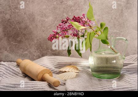 Lilacs in piccola caraffa di vetro su asciugamano a strisce da cucina. Pioli e capesante. Foto orizzontale con spazio per la copia. Foto Stock