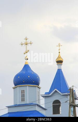 Chiesa cristiana ortodossa con pareti bianche, cupole blu e croci dorate in Russia. Un edificio per cerimonie religiose con un campanile contro un cielo nuvoloso in campagna. Foto Stock