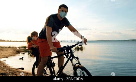 Uomo con bambino in bicicletta in maschere protettive Foto Stock