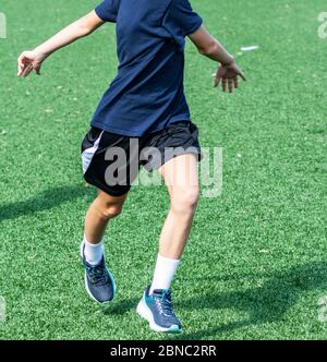 Un giovane atleta della scuola superiore sta eseguendo il kereoke che batte il trapano mentre si riscalda su un campo di erba durante l'esercitazione della squadra sportiva. Foto Stock
