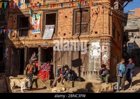 Dhulikhel, Nepal - 15 novembre 2016: Un gruppo di uomini e donne nepalesi sono seduti all'ingresso del negozio. Nelle vicinanze ci sono i cani. Foto Stock