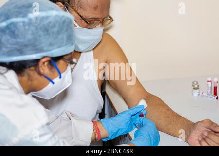 Nurse prende il campione di sangue di un maschio indiano anziano per l'esame del sangue medico alla luce della pandemia di coronavirus Foto Stock