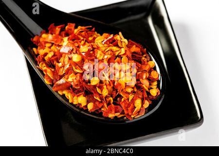 Da sopra cucchiaio di ceramica con scaglie di pepe rosso macinato posto su piastra quadrata su fondo bianco Foto Stock