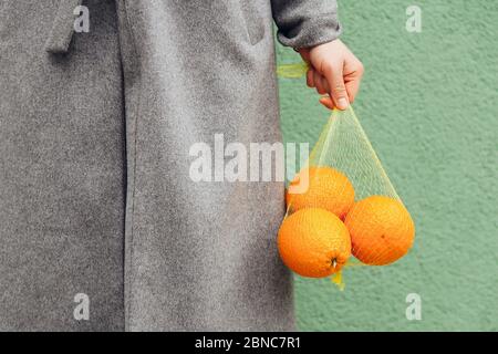 Donna tiene fresche Orange in plastica Mesh Sack su sfondo verde Foto Stock