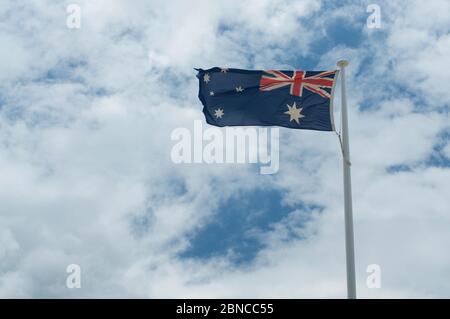 Bandiera australiana che oscilla nel vento forte, contro un cielo blu nuvoloso Foto Stock
