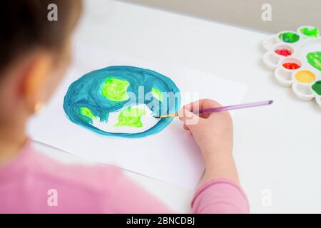 Bambino disegna un pianeta Terra con una mappa del mondo da acquerelli su carta bianca. Concetto di giorno della pace e della Terra. Foto Stock