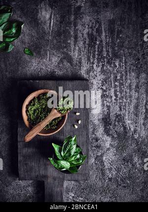 Salsa al pesto di basilico verde, parmigiano, aglio, pinoli in ciotola rustica di legno con cucchiaio su fondo ruvido scuro Foto Stock