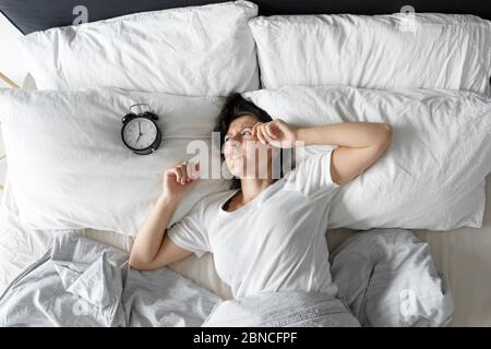 Vista dall'alto. La ragazza dorme accanto alla sveglia. Tentativo di disattivare la sveglia che interferisce con la modalità di sospensione. Tempo di attivazione. Profondo Foto Stock