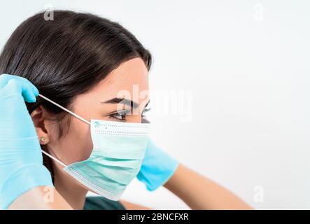 Giovane donna medico ritratto indossando maschera chirurgica viso e guanti - persone che lavorano per prevenire e fermare la diffusione del virus corona Foto Stock