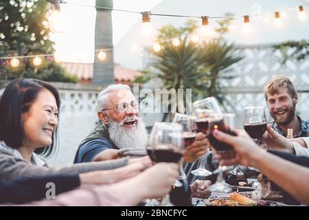 Happy cena in famiglia e tostatura bicchieri di vino rosso all'aperto - persone di età ed etnia diverse divertirsi con barbecue cena festa