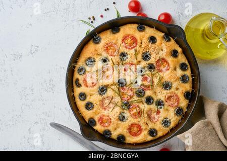 Focaccia, pizza in padella, pane italiano piatto con pomodori, olive e rosmarino. Vista dall'alto, spazio di copia, sfondo bianco in cemento Foto Stock