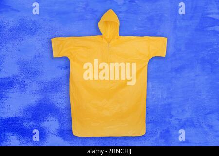 Cappotto piovoso giallo con cappuccio su sfondo blu stainy. Vista dall'alto Foto Stock