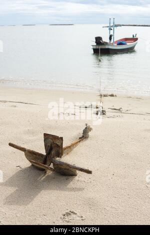 Vicino al vecchio Anchor sulla spiaggia. Piccola barca da pesca in legno ancorata sulla spiaggia. Foto Stock