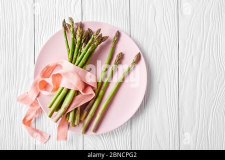 asparagi verdi freschi su un piatto rosa su un tavolo di legno bianco, piatto, spazio libero Foto Stock