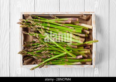 primo piano di asparagi verdi freschi non cotti in una scatola rustica di legno su un tavolo di legno bianco, piatto Foto Stock