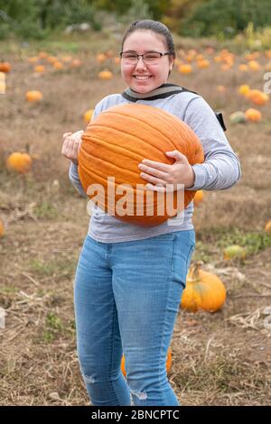 Una ragazza che porta una zucca grande in una fattoria Foto Stock