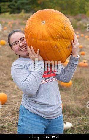 Una ragazza che porta una zucca grande in una fattoria Foto Stock