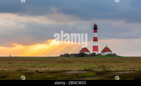 Il sole splende attraverso un buco nelle nuvole quasi direttamente sul faro. Foto Stock