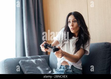 KIEV, UCRAINA - 9 APRILE 2020: Ragazza sorpresa giocando video gioco con joystick su auto isolamento Foto Stock