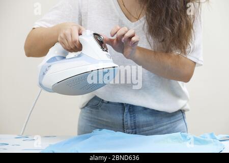 Giovane casalinga caucasica che stira i copriletti blu. Ragazza giovane facendo bucato e stirare vestiti dopo. Foto Stock