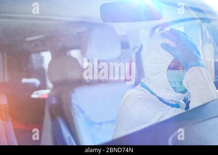 Esaurimento di una medica ambulanza in indumenti protettivi in ambulanza durante la pandemia di coronavirus Foto Stock