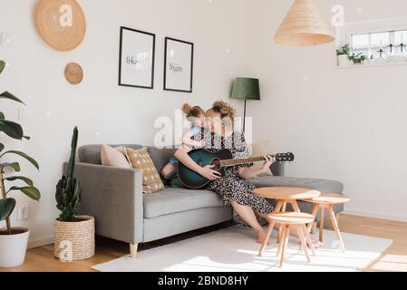 figlia baciare la mamma mentre suona la chitarra a casa Foto Stock