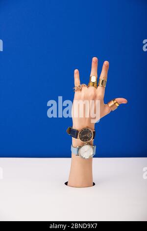vista della donna con orologio da polso a portata di mano e anelli dorati isolati in blu Foto Stock