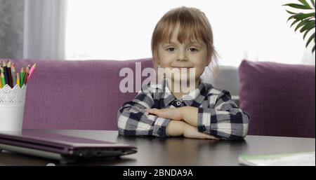 Pretty preschool ragazza distanza online imparare a casa. Carino bambino che studia a tavola utilizzando un computer portatile digitale, facendo compiti. Bambini formazione remota in quarantena Foto Stock