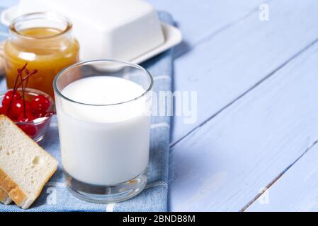 bicchiere di latte con miele e pane su sfondo di legno azzurro. Concetto di cibo per colazione country. Foto Stock