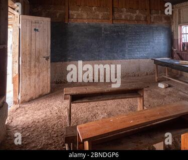 Tipica scuola povera in Kenya con pavimento sporco e vecchie scrivanie di legno Foto Stock
