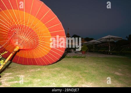 La luce illumina il rosso luminoso e l'arancione tradizionale ombrello asiatico a terra con sfondo scuro e cielo dietro. Foto Stock