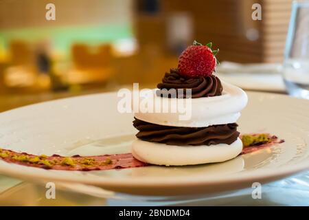 Torta meringa con cioccolato fondente e fragola sulla parte superiore, in ambiente arestaurant, con sfondo sfocato Foto Stock