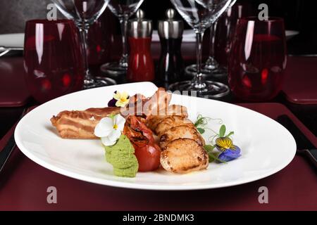 Capesante, pancetta, pera e purea di menta serviti su un piatto bianco in un ambiente ristorante. Menu gourmet raffinato, vista dall'alto e spazio per la copia Foto Stock