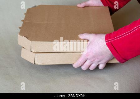 Due scatole di cartone chiuse per pizza a mani maschili. Un uomo in una T-shirt rossa contiene scatole per pizza. Consegna dei prodotti. Vista laterale. Foto Stock