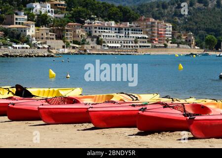 Kayak rossi allineati sulla spiaggia di Port de Soller, Maiorca, pronti per essere portati fuori da visitatori avventurosi Foto Stock