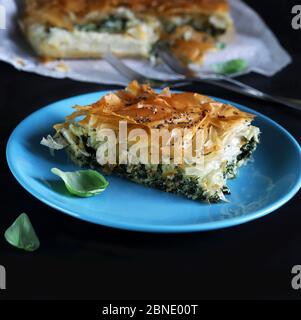 Cucina greca tradizionale. Spanakopita, un pezzo di torta di pasta frolla greca con spinaci e formaggio feta ripieno su piatto blu. Foto Stock