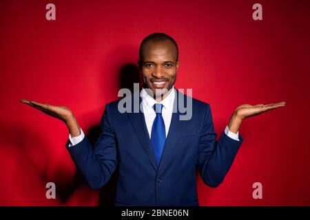 Foto di bel ragazzo di affari pelle scura attraente che tiene due braccia aperte dimostrando novità prodotti indossare blu tuta tuta tuxedo isolato Foto Stock