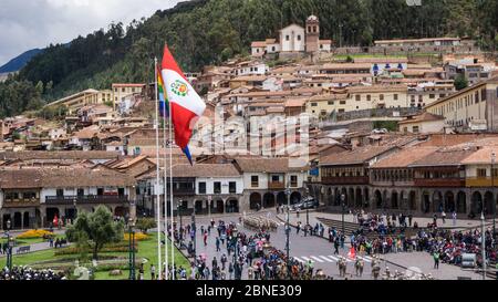 Bandiera peruviana nazionale accanto alla bandiera lgtb arcobaleno di fronte a un villaggio con vecchi edifici che salgono su una collina di montagna di fronte a una strada affollata Foto Stock