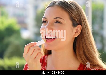 Donna giovane sorridente che applica protezione solare sul labbro all'aperto Foto Stock