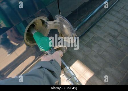 Una mano dell'uomo tiene una pistola di rifornimento verde. Pistola di riempimento inserita nel foro di un serbatoio di benzina vuoto di un'auto con un carburante diesel Foto Stock