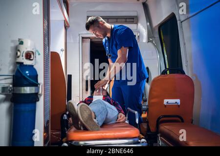 Giovane paramedico che dà una maschera di ossigeno alla sua paziente femminile in un'auto ambulanza Foto Stock