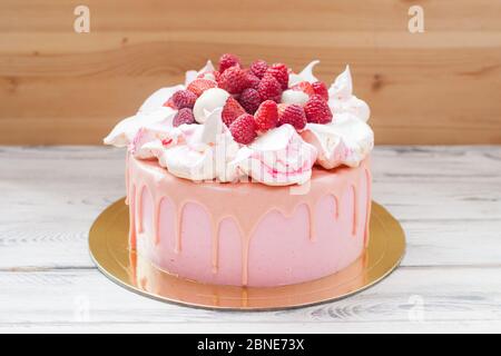 Torta al formaggio rosa con cioccolato fuso, meringhe, lamponi freschi e fragole. Sfondo di legno. Foto Stock