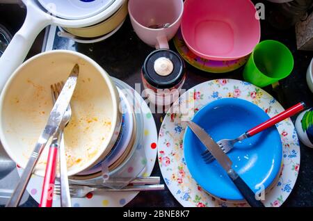 Lavaggio - piatti, piatti, coltelli, forcelle, tazze impilate su un piano di lavoro da cucina pronti per la pulizia. Foto Stock