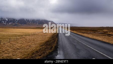 Autostrada campagna dritto strada vuota che conduce alle montagne innevate nella penisola di snaefellsnes in Islanda Foto Stock