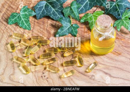 Capsule oblunghe gelatinose trasparenti di olio di pesce sono state sparse sullo sfondo di legno. Acidi grassi polinsaturi essenziali Omega-3-in linseed o Foto Stock